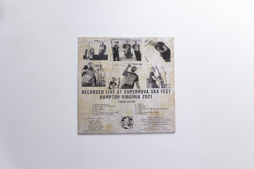 A square printed cover or poster mounted against a plain light gray wall. The artwork has a distressed beige background with multiple small black-and-white photos arranged in a collage, plus black text reading 'RECORDED LIVE AT SUPERNOVA SKA FEST HAMPTON VIRGINIA 2021' and additional track/artist text below.
