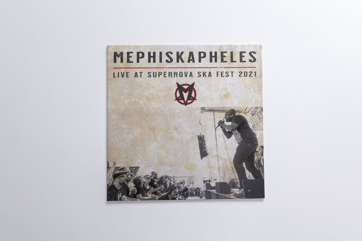 A square album or print cover for Mephiskapheles titled 'Live at Supernova Ska Fest 2021', shown hanging against a plain light gray wall. The cover has a distressed beige background with black text, a red logo, and a black-and-white photo of a performer on stage.