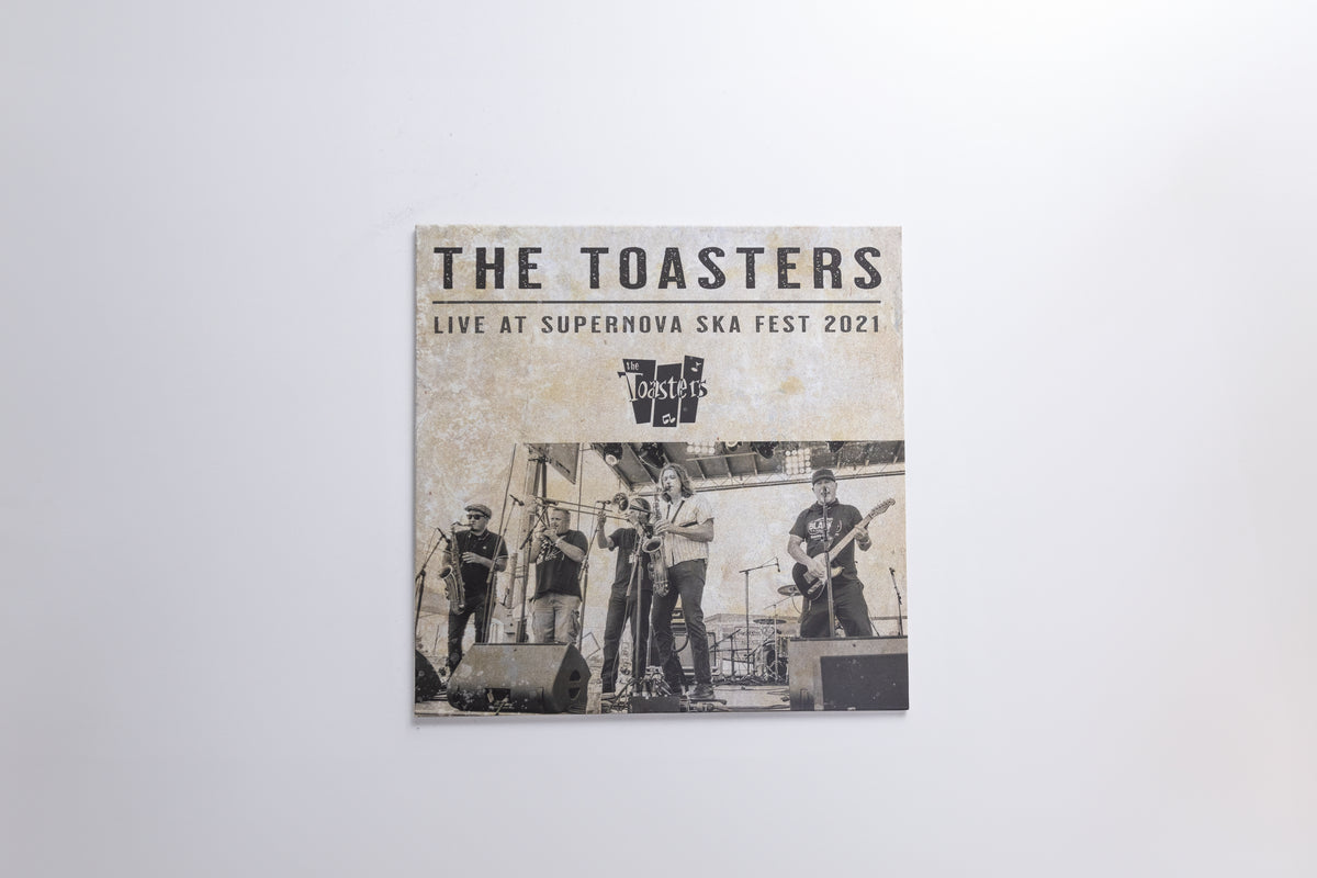 A square printed cover or poster for 'The Toasters Live At Supernova Ska Fest 2021' hangs against a plain light gray wall. The artwork shows a band performing on stage in a sepia-toned photo with black text at the top.